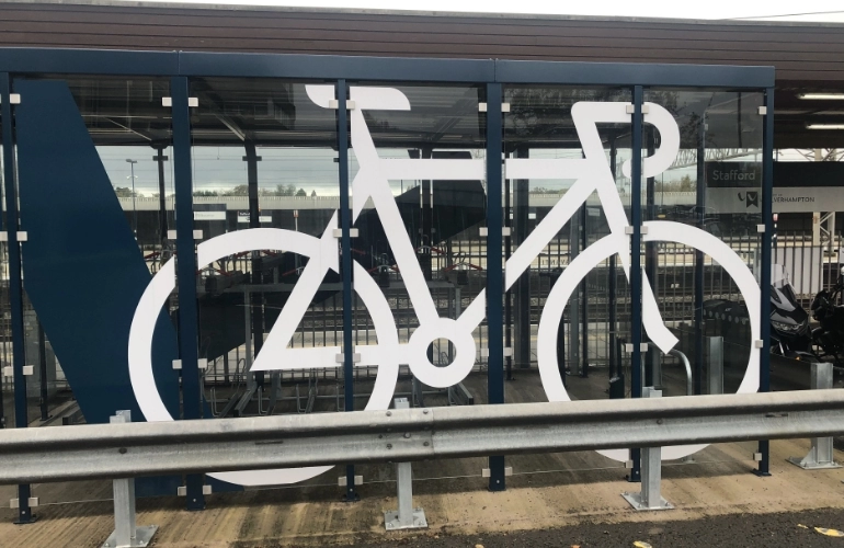 Wiata rowerowa z przeszkloną ścianą i oznaczeniem roweru